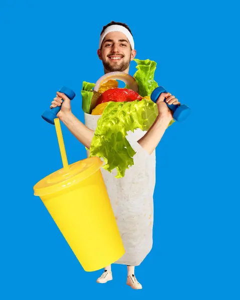Young smiling man training, doing exercises and eating shawarma over blue background. Contemporary art collage. Fitness center, diet and nutrition. Concept of pop art, food services. Poster, ad