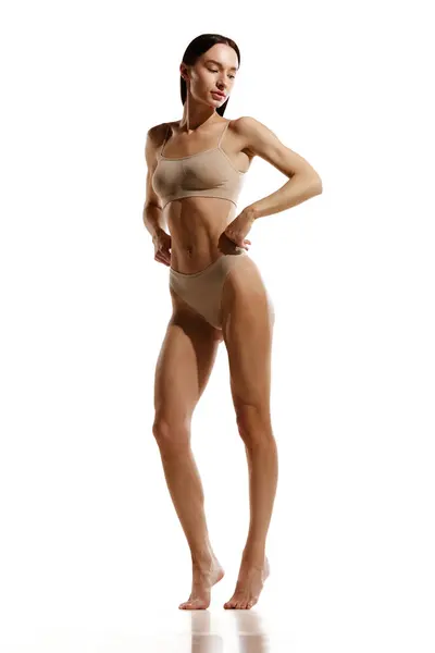 フィットネスプログラム 白いスタジオの背景に対してベージュの綿の下着にポーズするスリム フィット 筋肉体を持つ若い女性 女性の美しさ 体とスキンケア 化粧品 スポーツ 健康の概念 ロイヤリティフリーのストック画像