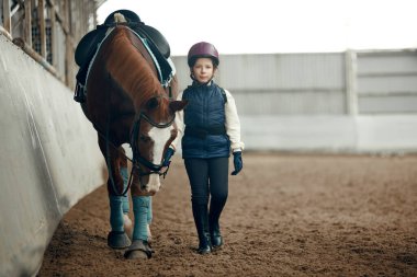 Küçük bir kız, özel üniformalı bir çocuk ve at binme eğitimi sırasında atıyla yürüyen bir kask. Hayvan davranışları ve bakımı. Spor, çocukluk, okul, aktif yaşam tarzı, hobi konsepti