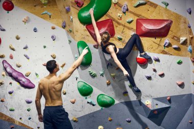 Kaslı üstsüz genç bir adam, kaya talimi yapıyor genç bir kıza duvara tırmanmayı öğretiyor. Spor karşılaşması. Spor, kaya, spor tırmanışı, hobi, aktif yaşam tarzı, okul, eğitim kursu kavramı