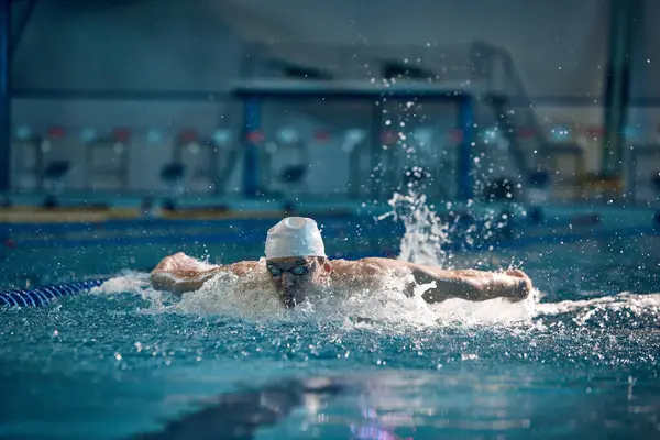 Butterfly swimming techniques. Athletic young man in motion, training, swimming in pool, wearing cap and goggles. Concept of pool sports, water sport, competition, active lifestyle