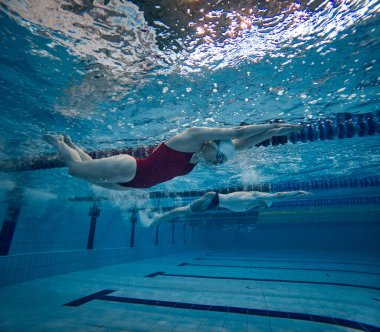 Su altında yüzmek. Kırmızı mayo, kep ve gözlük takan, antrenman yapan, havuzda yüzen genç bir kız. Havuz sporları, su sporları, rekabet, aktif yaşam tarzı kavramı