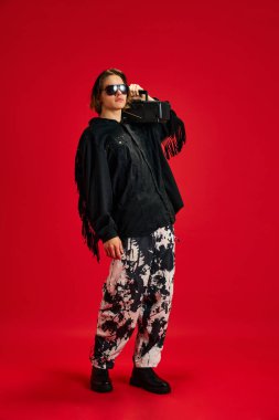 Kırmızı stüdyo arka planında klasik teypten popüler müzik dinleyen genç ve iyi giyimli bir adamın tam boy portresi. Hobi, retro, moda ve tarz kavramı, kendini ifade etme. Ad
