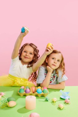 Güzel küçük kızlar ellerinde pembe arka planda süslü Paskalya yumurtaları tutuyorlar. Hazırlık. Paskalya tatili kavramı, kutlama, gelenekler, çocukluk, mutluluk