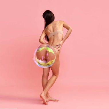 İnce vücutlu, kalçaları sabun köpüğü olan genç bir kadının arka plan görüntüsü. Pembe arka planda iç çamaşırlı bir model. Kadın güzelliği, vücut ve cilt bakımı, kilo kaybı, diyet