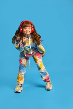 Down sendromlu, kulaklık takan, mikrofonu delen ve mavi arka planda şarkı söyleyen mutlu bir kız. Hobi olarak. Kabul, bakım, kapsama, sağlık, çeşitlilik, duygular, eşitlik kavramı