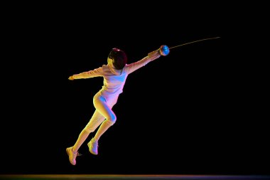 Spor eğitimi. Sporcu kendini spora adamış bir sporcu olarak kendini geliştirdi. Siyah arka planda hareket halinde olan neonlu bir kadın eskrimci. Spor, rekabet, şampiyonluk kavramı