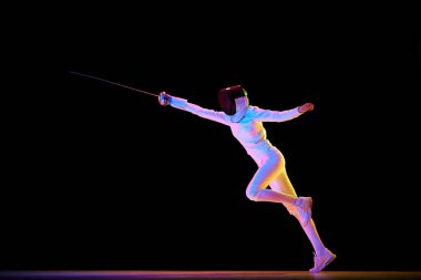 Tam teçhizatlı bir eskrimci, hassas bir şekilde saldırıyor, neondaki siyah arka planda izole edilmiş. Hareket halindeki kadın sporcu, kılıç eğitimi alıyor. Profesyonel spor, rekabet, şampiyonluk, başarı konsepti