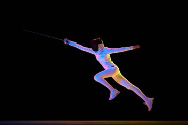 Spor eğitimi. Sporcu kendini spora adamış bir sporcu olarak kendini geliştirdi. Siyah arka planda hareket halinde olan neonlu bir kadın eskrimci. Spor, rekabet, şampiyonluk kavramı