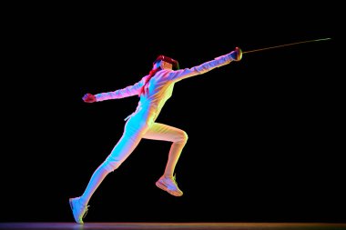 Hareket ve hareket. Yüksek hızlı bir fotoğrafta yakalanan bir atletin dinamik hareketi. Neon rengi siyah arka plan üzerine kadın eskrim eğitimi. Profesyonel spor, rekabet, şampiyonluk kavramı