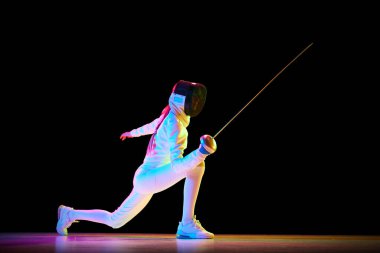 Güç ve zarafet. Eskrim sanatında güç ve zarafet kombinasyonu gereklidir. Kadın sporcu, eskrimci neon ışıkta siyah arka planda hareket halinde. Spor anlayışı, rekabet, hobi