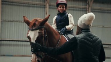 Genç bir kadın, öğretmen, eğitmen küçük kıza ata binmeyi öğretiyor. Çocuk kürek çekiyor, pratik yapıyor. Eğitim. Spor, çocukluk, okul, kurs, aktif yaşam tarzı ve hobi kavramı