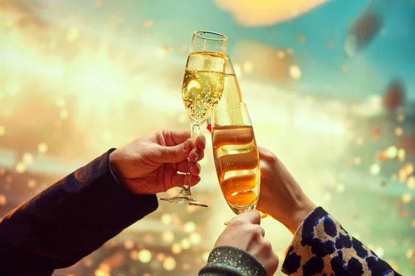 New Years Eve party invitation card design featuring a champagne toast. Hands clinking champagne flutes with sparkling liquid over a bokeh light background. Concept of holidays, celebration, events