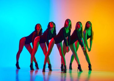 Yüksek topuklularla dans eden güzel, tutkulu genç kadınlar neon ışıklı sarı arka planda. Modern dans stili kavramı, yaratıcılık ve güzellik, sanat, hobi