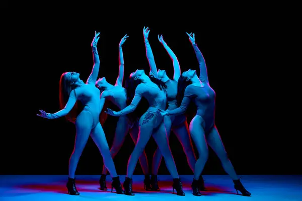 Group of artistic young women, dancers in bodysuits and heeled shoes performing against black background in neon light. Concept of modern dance style, creativity and beauty, art, hobby