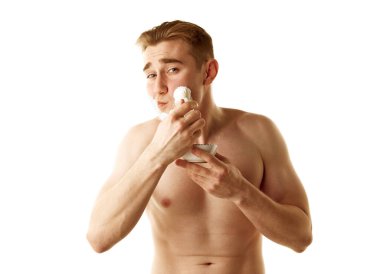 Gömleksiz genç adam tıraş oluyor, yüzüne tıraş kremi sürüyor beyaz arka planda izole edilmiş halde. Yumuşak bir ten. Erkek güzelliği, cilt bakımı, kozmetik ve kozmetik ürünleri, sağlık