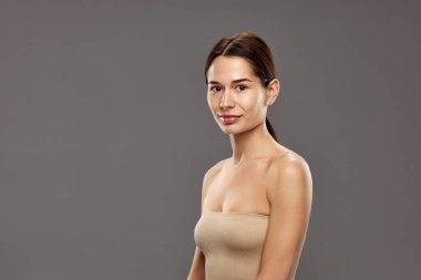 Makyajsız, at kuyruklu, stüdyo arka planında askısız bluz giyen güzel bir kadının profil görüntüsü. Doğal güzellik kavramı, kozmetik ve kozmetik, cilt bakımı