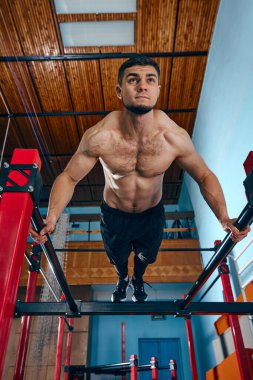 Güçlü vücudu olan kaslı, atletik genç bir adam, spor salonunda üstsüz antrenman yapıyor, paralel barlarda şınav çekiyor. Aktif ve sağlıklı yaşam tarzı kavramı, vücut bakımı, fitness, spor