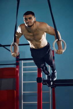 Güçlü rahatlamış vücudu olan kaslı, atletik genç adam spor salonunda jimnastik yüzükleriyle Ring Push Up yapıyor. Aktif ve sağlıklı yaşam tarzı kavramı, vücut bakımı, fitness, spor