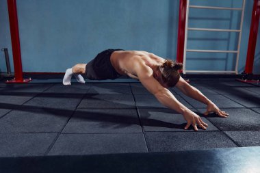 Güçlü, kaslı, spor salonunda üstsüz vücut antrenmanı yapan esneme ve kalas egzersizleri yapan atletik bir genç. Aktif ve sağlıklı yaşam tarzı kavramı, vücut bakımı, fitness, spor