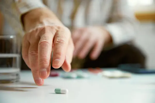 Close-up of male hands taking pills, vitamins, meds at home. Blurred background, focus on hands. Concept of health and medical care, aging, medicine, treatment