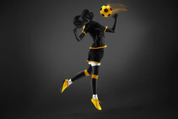 Competitive young woman, soccer player in uniform in motion, playing, hitting ball with chest over dark background. Yellow elements. Concept of competition, tournament, match, game. Creative design.