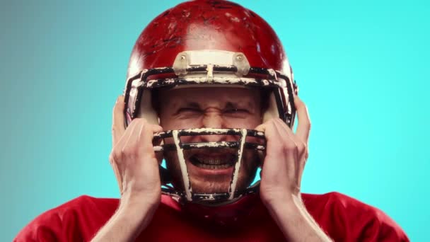 赤いフットボールのヘルメットの男 アメリカのサッカー選手は感情的に激しい感情を表現し 青い背景に対して叫びます プロスポーツ 大会のコンセプト — ストック動画