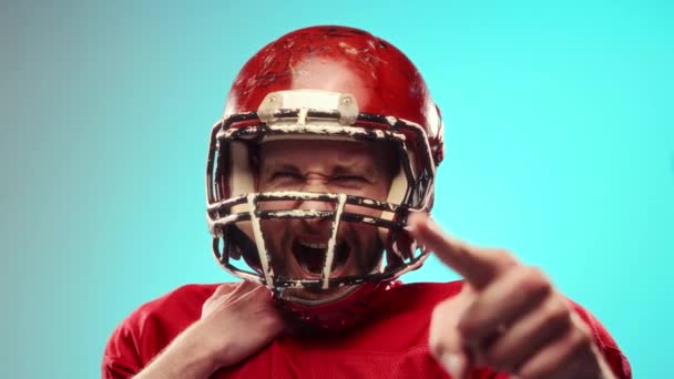 ゲームスピリット 感情的な若いアメリカンフットボール選手 ヘルメットと赤いユニフォームの男は再び青い背景を叫びます チャンピオン プロスポーツ 大会のコンセプト — ストック動画