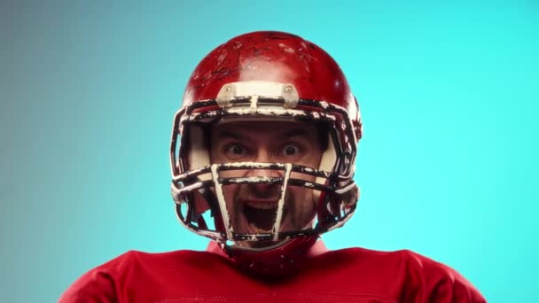 ゲームを続ける アミリアンフットボール選手は 赤いユニフォームと感情的にヘルメットし 青い背景に対して集中的に叫びます プロスポーツ 大会のコンセプト — ストック動画
