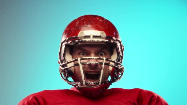 アメリカンフットボール選手の激しい感情は 青い背景に対して叫び声を上げます 赤いユニフォームとヘルメットを着ている男 プロスポーツ コンペ トーナメントのコンセプト — ストック動画