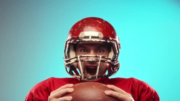 比赛前表现出的能量情绪化的男人 戴着头盔 身穿红色制服的美式足球运动员 拿着球 在蓝色背景下大喊 职业体育 锦标赛概念 — 图库视频影像