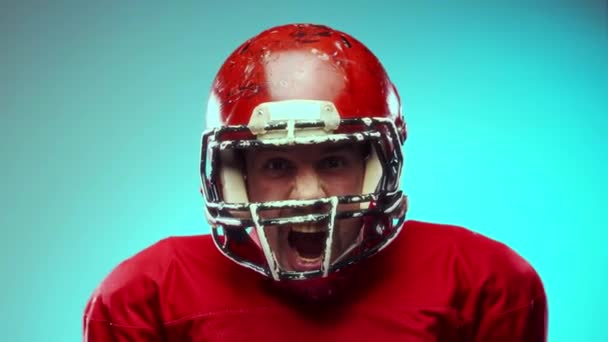 感情的な男 ヘルメットと赤いユニフォームのアメリカのサッカー選手 ボールが叫び 青い背景に対してヘルメットをノック プロスポーツ 大会のコンセプト — ストック動画