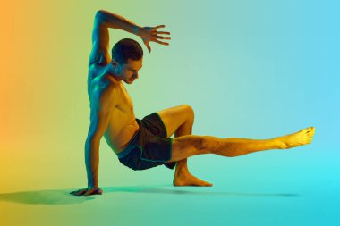 Kaslı, rahatlatıcı, güçlü vücut eğitimi almış genç bir adam, neon ışıkta sarı arka plana karşı egzersiz yapıyor. Aktif ve sağlıklı yaşam tarzı kavramı, spor, fitness