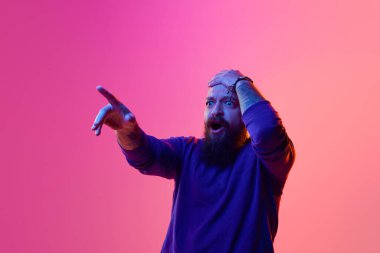 Vay canına. 30 'larında sakallı kel bir adam ağzı açık, gözleri açık, şok olmuş yüzünü gösteriyor ve neon ışıkta pembe arka planı işaret ediyor. İnsan duyguları kavramı, yüz ifadesi