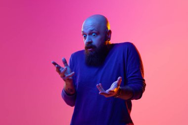 Kel sakallı adamın portresi, neon ışıkta pembe arka plana karşı şok olmuş yüzüyle duygularını ifade ediyor. İnsan duyguları kavramı, yüz ifadesi, haberler