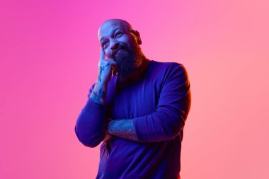 Düşünceli sakallı bir adam, eli yüzünde pembe arka plandaki duyguları neon ışıklarıyla ifade ediyor. Seçim yapıyorum. İnsan duyguları kavramı, yüz ifadesi