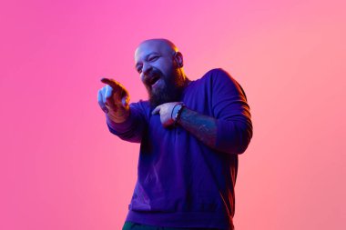 30 'larında, sakallı ve kel bir adam ileri doğru bakıp gülüyor, neon ışıkta pembe arka planla dalga geçiyor. İnsan duyguları kavramı, yüz ifadesi, eğlence ve neşe