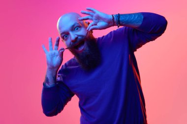 Mavi kazaklı sakallı kel adamın jel portresi duygularını ifade ediyor, neon ışıkta pembe arka planda yüzünü buruşturuyor. İnsan duyguları kavramı, yüz ifadesi