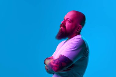 Sıradan beyaz tişörtlü sakallı kel bir adamın portresi, düşünceli bir şekilde duruyor. Neon ışıkta mavi arka planda rüya gibi bir yüz. İnsan duyguları kavramı, yüz ifadesi