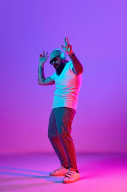 Gündelik giysiler içinde, kulaklıkla müzik dinleyen, sakallı kel bir adamın tam boy görüntüsü neon ışıkta mor bir arka planda. İnsan duyguları kavramı, yüz ifadesi