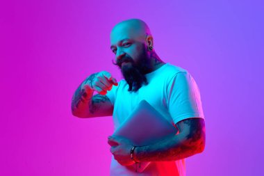 Diz üstü bilgisayarı olan sakallı kel bir adam neon ışıkta parmak ucunda mor bir arka plan görüyor. İstihdam, serbest işler. Adam topluyorum. İnsan duyguları kavramı, yüz ifadesi