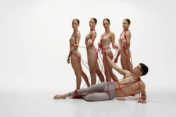 芭蕾艺术 男舞蹈演员躺在地板上 四个女舞蹈演员站在旁边 她们的背景都是白色的 用红线连接在一起 古典舞的概念 现代风格 — 图库照片
