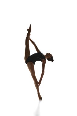 Esnek bir genç kızın tam boy görüntüsü, zarif sahne kostümlü ritmik jimnastikçi beyaz stüdyo arka planında gösteri yapıyor. Spor, güzellik ve zarafet kavramı, rekabet, sanat, gençlik, hobi