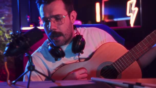 Mann Mit Kopfhörer Spielt Akustikgitarre Neben Mikrofon Neonbeleuchteten Studio Aufnahme — Stockvideo