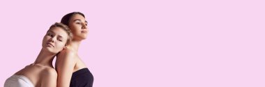 Pembe arka planda duran, bakımlı, sağlıklı ciltli ve çıplak makyajlı iki güzel kızın portresi. Güzellik, bakım, kozmetik ve kozmetik kavramı. Pankart. Metin eklemek için boş boşluk, ad