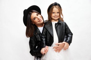 Güzel genç bir kadın, annesi küçük kızıyla aynı tarz kıyafetlerle beyaz stüdyo geçmişine karşı poz veriyor. Mutluluk kavramı, anneler günü, çocukluk, moda ve yaşam tarzı.