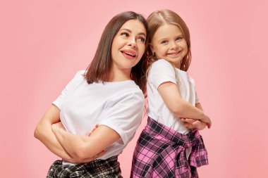 Destek ve bakım. Pembe stüdyo geçmişine karşı küçük kızla sırt sırta duran mutlu genç bir kadın. Anne-kız kaynaşıyor. Mutluluk kavramı, anneler günü, çocukluk, moda.