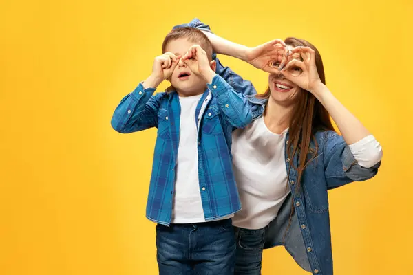 Playful happy family. Mother spending good timer with her little son, playing and laughing against yellow studio background. Concept of happiness, Mothers day, childhood, fashion and lifestyle