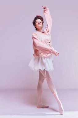 Güzel, hoş elbiseli genç bir kadın yine balerin gibi dans ediyor. Pastel pembe arka plan. Hobi, estetik. Güzellik ve moda kavramı, eski moda, yatak odası tarzı