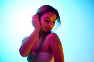 Atkuyruklu zarif bir genç kız, beyaz bir operasyon giyiyor, neon ışıklarıyla arka plandaki gradyan stüdyoya karşı duruyor. Güzellik kampanyası. Güzellik, cilt bakımı, kozmetik ve kozmetik kavramı